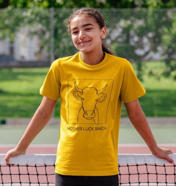 girl wearing the Cowabunga! shirt showing a cow sketch with text "Mother Luck Ranch" in mustard