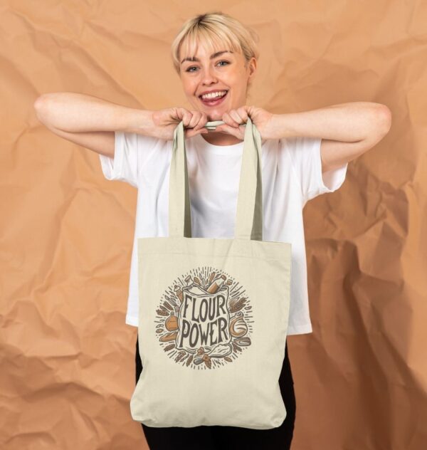 girl holding shopping tote bag in natural color featuring Flour Power design showing a flour sack and baking accessories