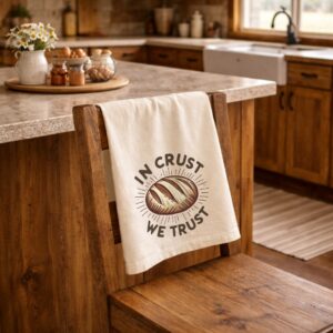 organic cotton dish towel in natural color with In Crust We Trust design hanging over kitchen chair