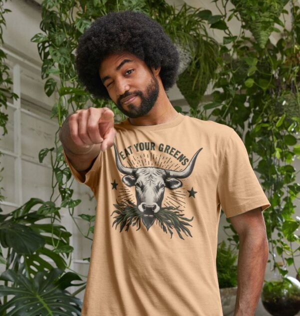 Man wearing the Men's Eat Your Greens Organic Cotton T-Shirt in Sand Color showcasing a steer eating greens