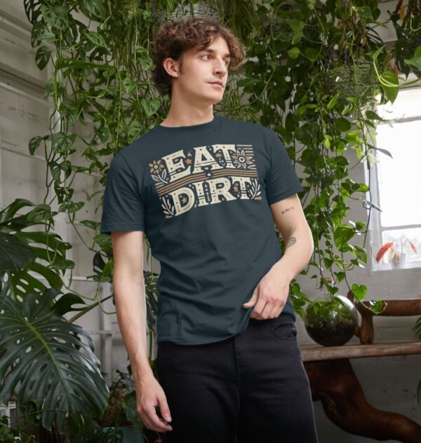 man surrounded by houseplants wearing the Eat Dirt Organic Cotton T-Shirt in Denim Blue Color