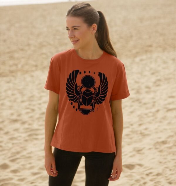 Woman on Beach Wearing the Winged Scarab Organic Cotton Relaxed Tee in Rust Color