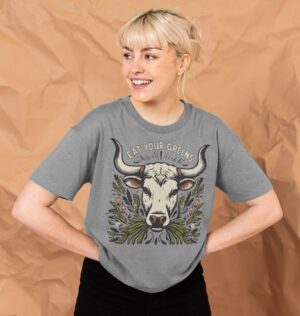 woman wearing the Women's Eat Your Greens Organic Cotton Boxy Tee in Athletic Grey showcasing a cow eating greens in folk art style motif