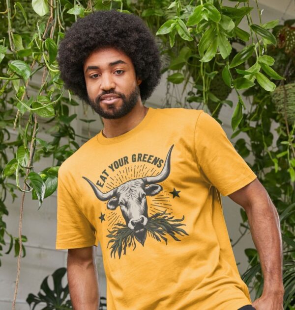 Man wearing the Men's Eat Your Greens Organic Cotton T-Shirt in Mustard Color showcasing a steer eating greens