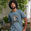 Man wearing the Men's Eat Your Greens Organic Cotton T-Shirt in Stone Blue Color showcasing a steer eating greens