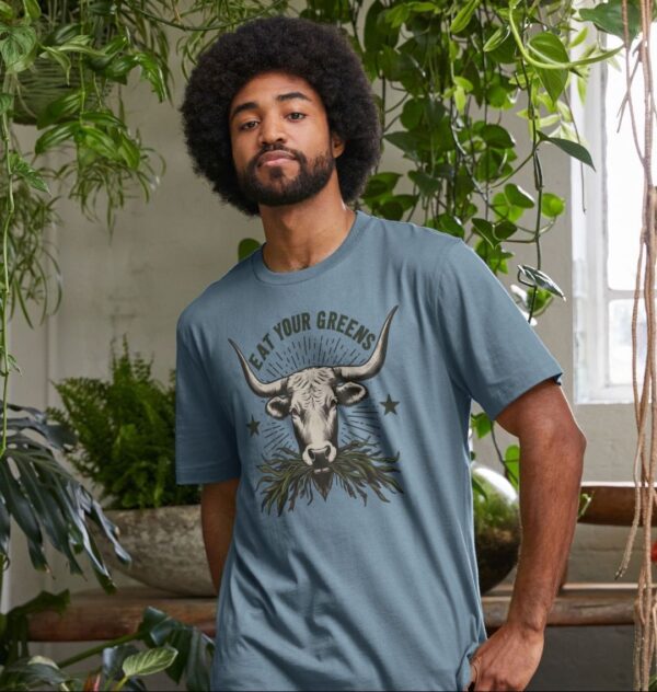 Man wearing the Men's Eat Your Greens Organic Cotton T-Shirt in Stone Blue Color showcasing a steer eating greens