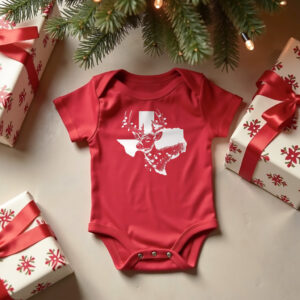 Red organic cotton baby onesie featuring Texas Christmas design in white with a sketch of a white tail deer wrapped in lights in front of the shape of Texas. Onesie is on the ground under a Christmas tree between wrapped presents.